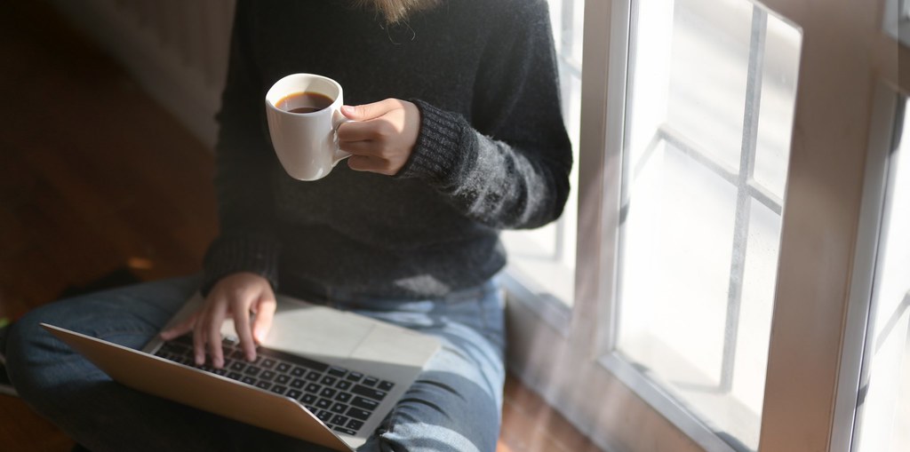 Woman using laptop while holding a cup of coffee - Credit to https://homegets.com/